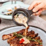 A Person Pouring Mushroom Sauce on the Roasted Meat